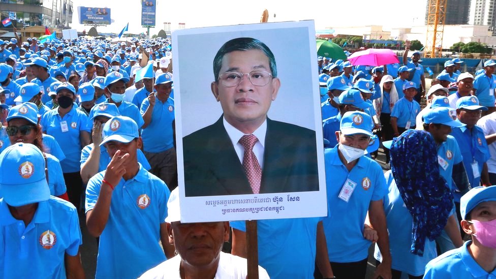 A crowd of ruling party supporters wearing blue uniforms and hats march in Phnom Penh on 1/7 in support of Hun Sen, with one carrying a large placard bearing the PM's picture