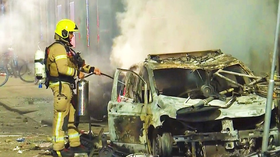 Un bombero apaga un auto incendiado en Rotterdam