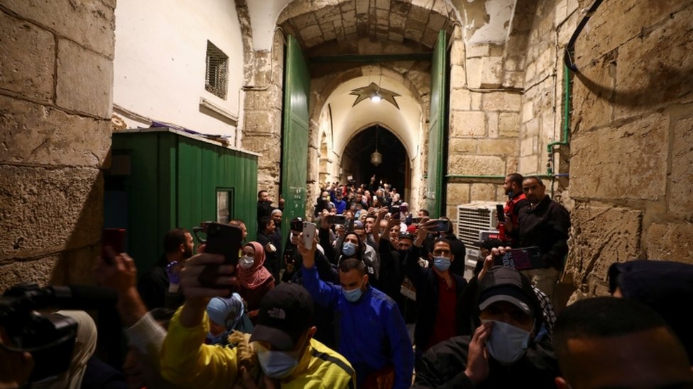 Worshippers, some wearing masks, hold up their mobile phones while entering the compound housing the Al-Aqsa Mosque