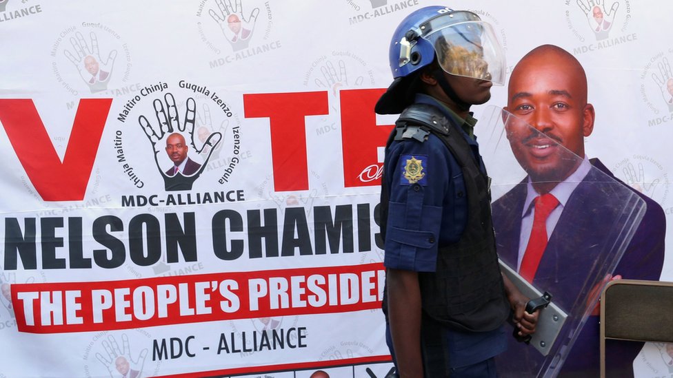 Un policía antimotines camina frente a una valla publicitaria de la Alianza MDC, en Harare, Zimbabue