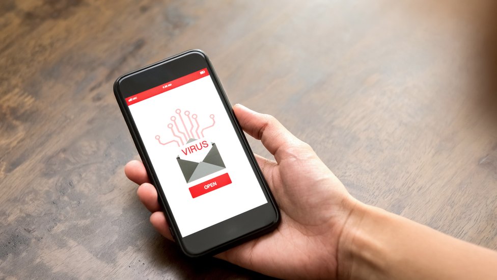 Mano sujetando celular con imagen de un correo electrónico infectado por un virus.