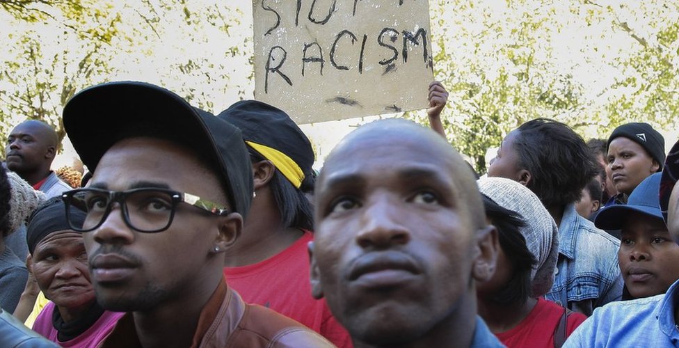 Протестующие в Южной Африке держат табличку с надписью "Стоп расизм"