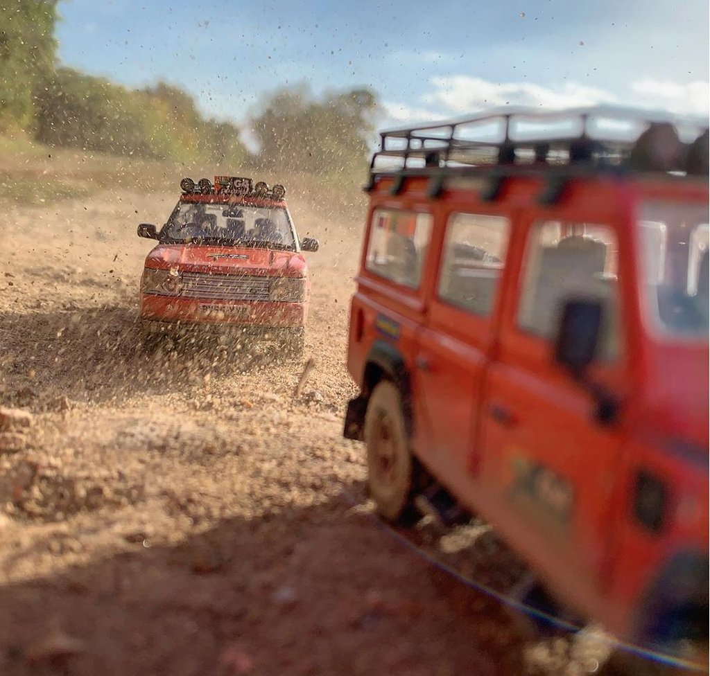 Красная модель Land Rovers едет по грунтовой дороге