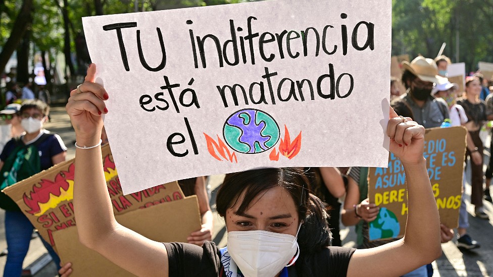 Joven en México con un cartel que dice: "Tu indiferencia está matando el planeta"