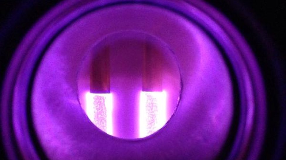Два светящихся плазменных стержня в изолированной камере создают пурпурное свечение