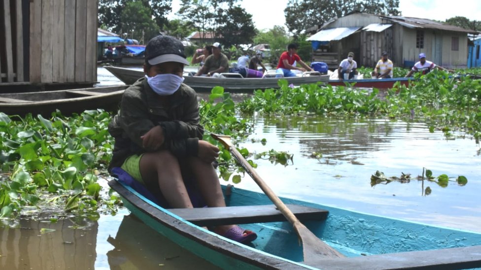 Joven con una mascarilla, sentado en una canoa en Leticia, Colombia