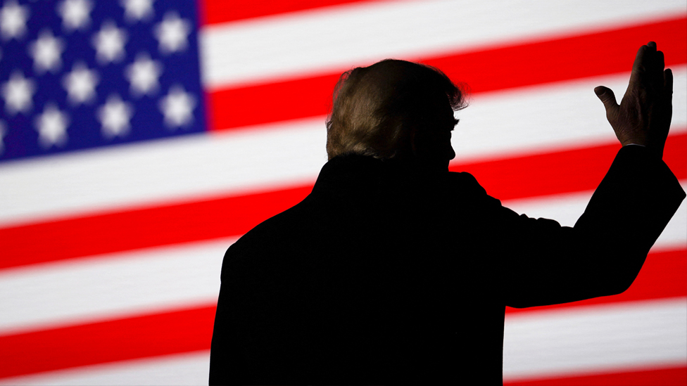 Donald Trump silhouetted against a US flag