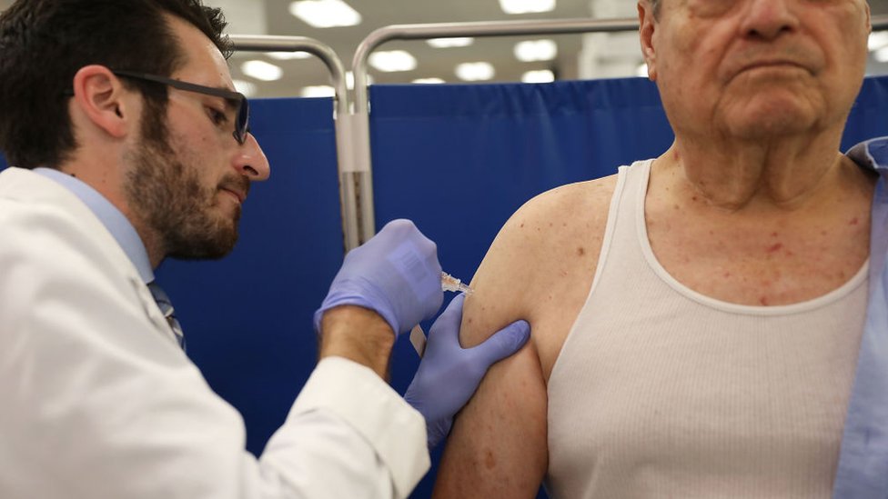 hombre poniendo una vacuna contra la influenza a otro hombre