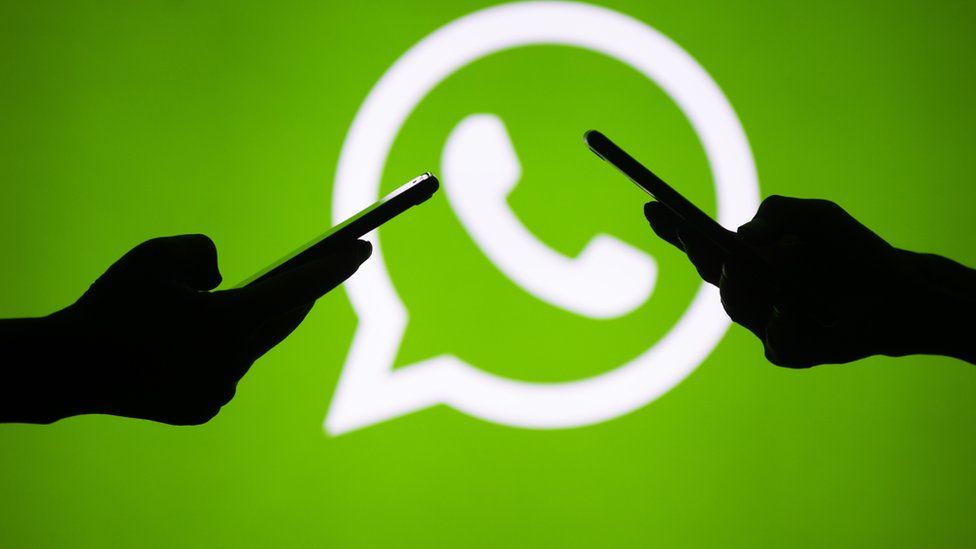 Sombra de dos personas manejando celulares con el logo de WhatsApp de fondo.