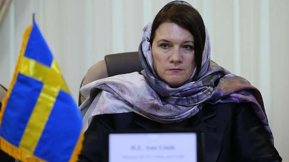 Энн Линде в светло-лиловом платке сидит за столом с маленьким шведским флагом в Тегеране, Иран