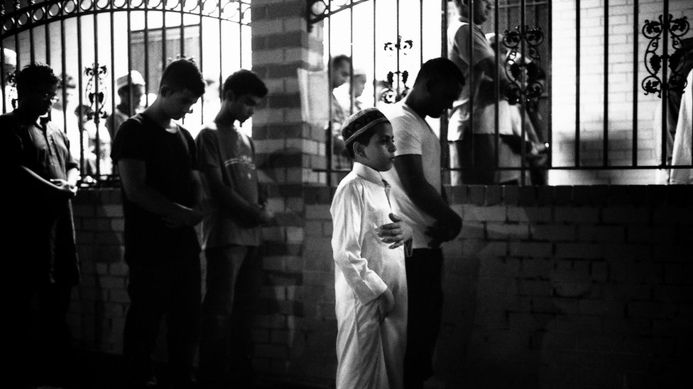 Niño rezando durante el Ramadán en la calle fuera de la mezquita porque la mezquita está llena, Parkchester Jame Masjid, en el Bronx, 2012. Niño rezando durante el Ramadán en la calle fuera de la mezquita porque la mezquita está llena, Parkchester Jame Masjid, en el Bronx, 2012.
