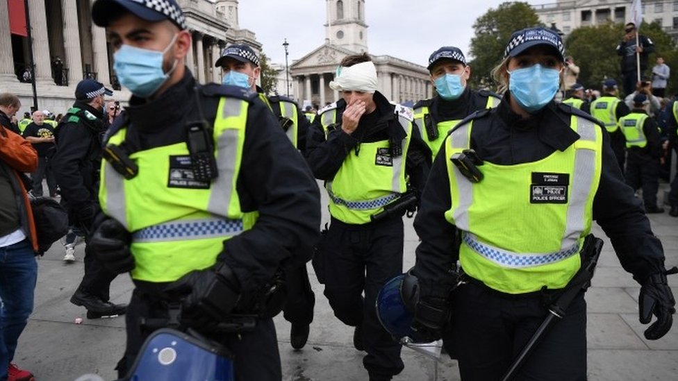 Раненому полицейскому помогают уйти после столкновения полиции с демонстрантами во время митинга «Мы не соглашаемся» в Лондоне