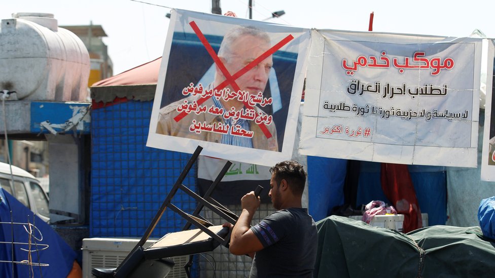 Иракский протестующий проходит мимо плаката с отказом от нового премьер-министра Мустафы аль-Кадими на площади Тахрир, Багдад, Ирак (7 мая 2020 г.)