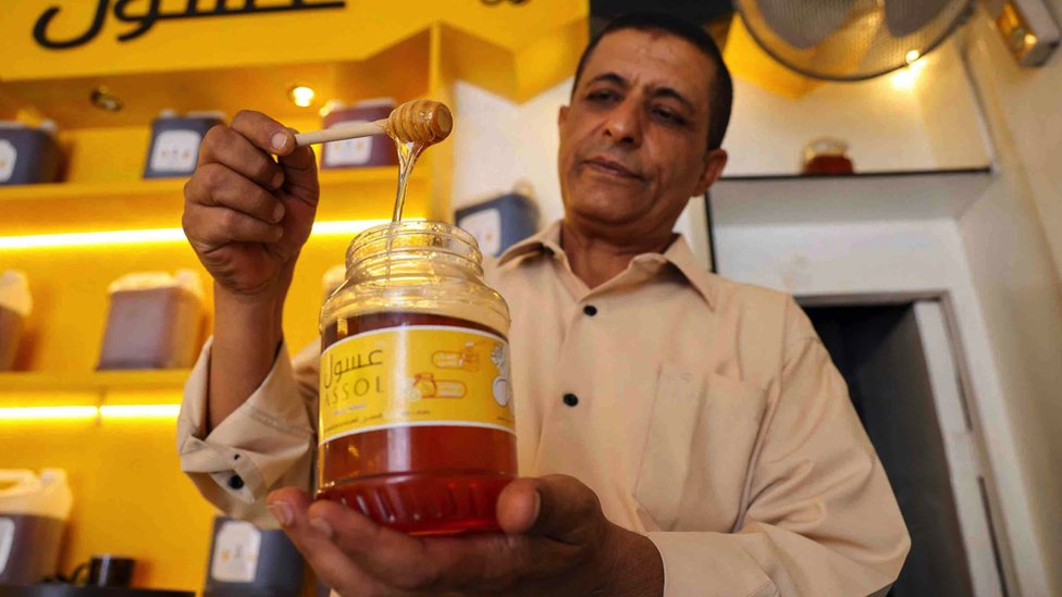 A Yemeni vendor scoops honey from a jar at his shop in Yemen's third city of Taez in June 2022s. The United Nations says honey plays a 