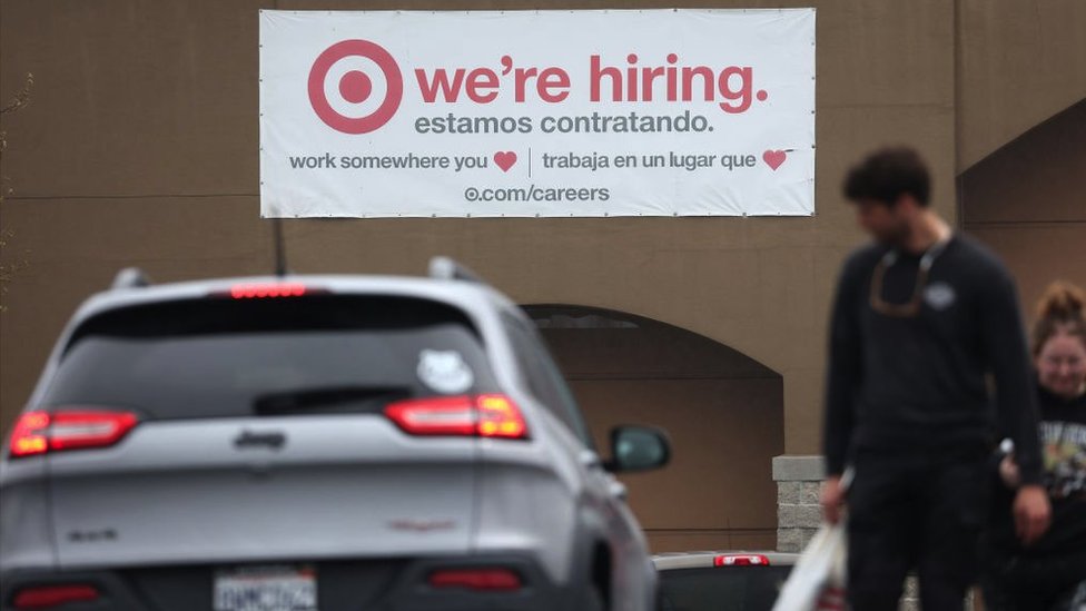 A sign in English and Spanish looking for employees in California