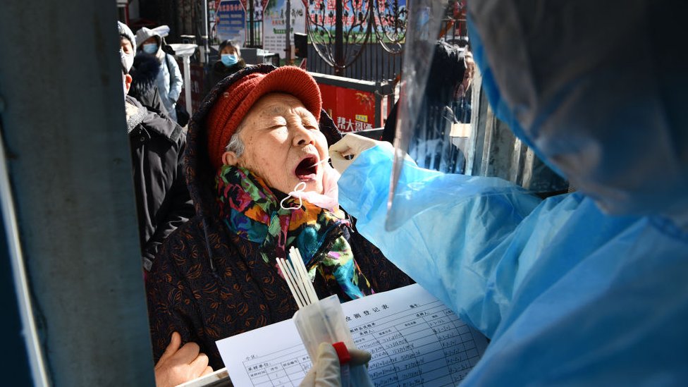 This photo taken on January 6, 2021 shows a medical worker taking a swab sample from a woman outside a residential compound following a new outbreak of the Covid-19 coronavirus in Shijiazhuang