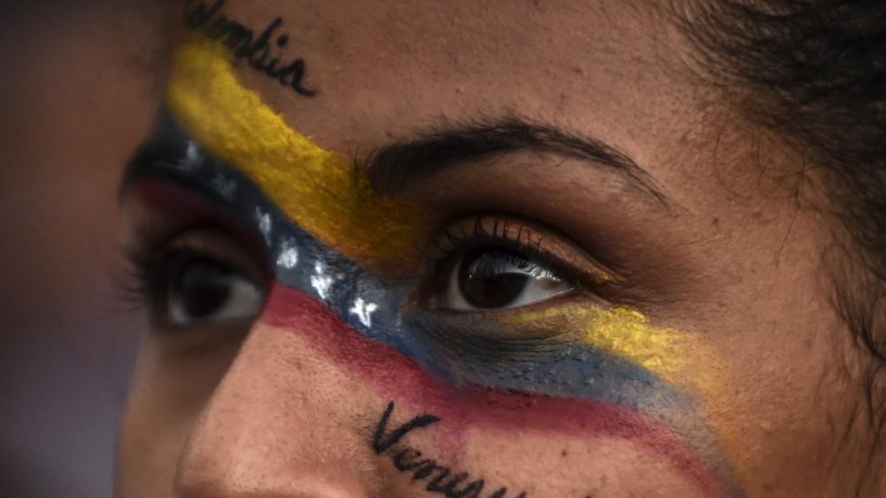 Imagen muy cerrada de los ojos de una mujer con la bandera colombiana y venezolana pintada en el rostro y las palabras "Colombia" y "Venezuela".