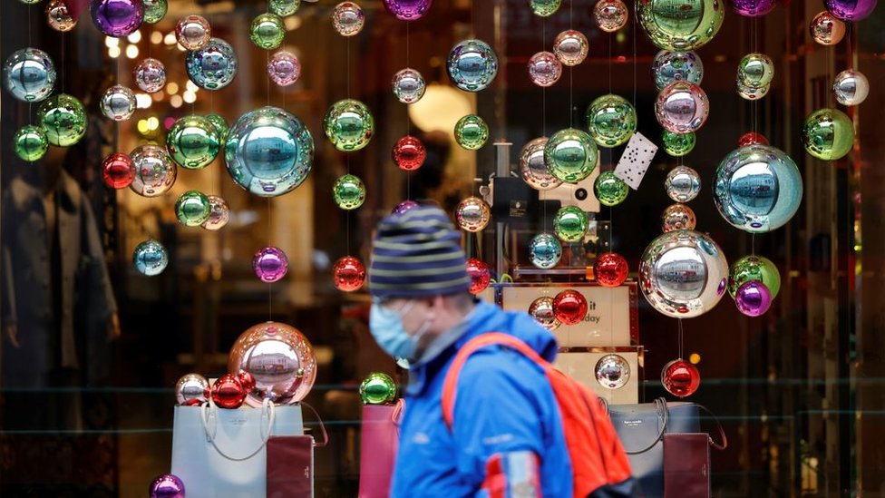 A man wearing a mask walks past a Christmas display
