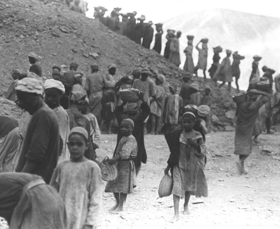 Foto em preto e branco mostra dezenas de trabalhadores egípcios na escavação em Luxor; muitos estão cobertos de poeira e há crianças entre eles