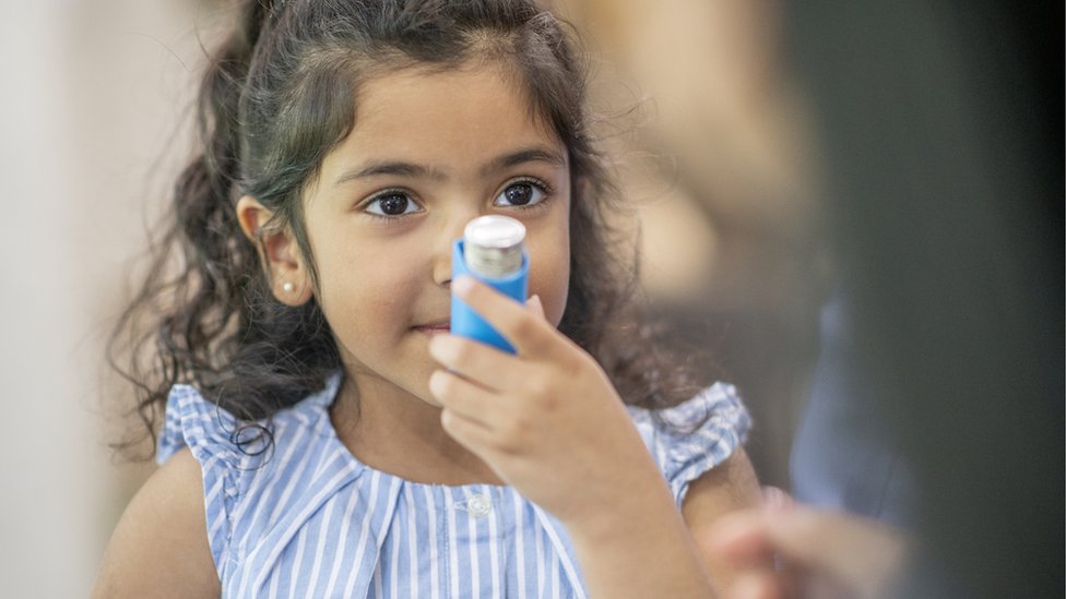 Menina criança segurando bombinha de asma em frente ao rosto