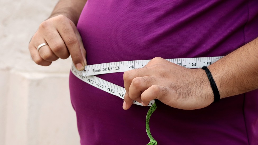 Persona con sobrepeso midiendo su barriga con un centímetro