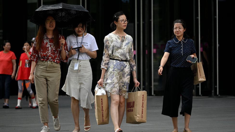A woman, carrying two shopping bags, walks out of a mall in Beijing on August 14, 2019