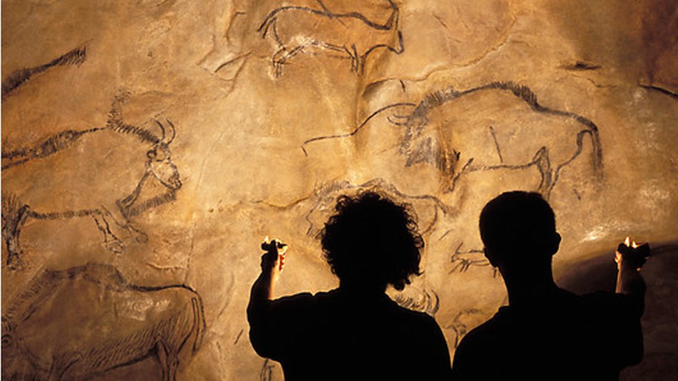 Силуэты двух человек, держащих масляные лампы для освещения наскальных рисунков