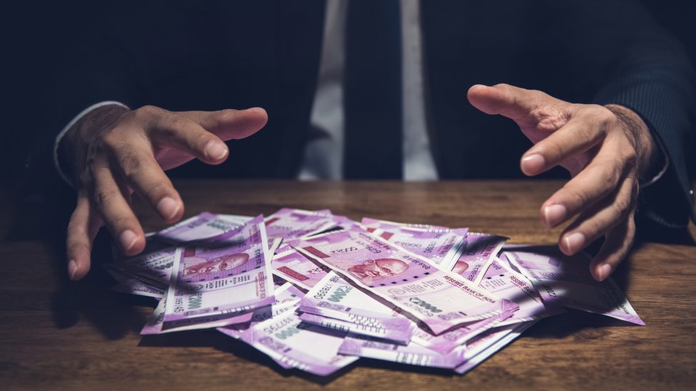 Бизнесмен принимает кучу денег, банкноты индийской рупии, на своем столе в темном офисе