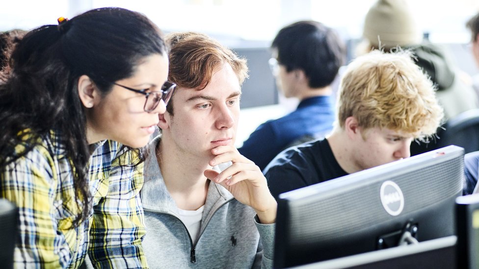 Three students - two male and one female - examine a computer screen in this photo