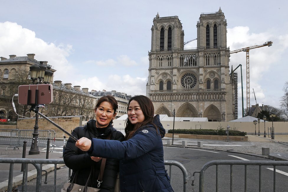 Tourists take a photo with the Notre-Dame cathedral in the background