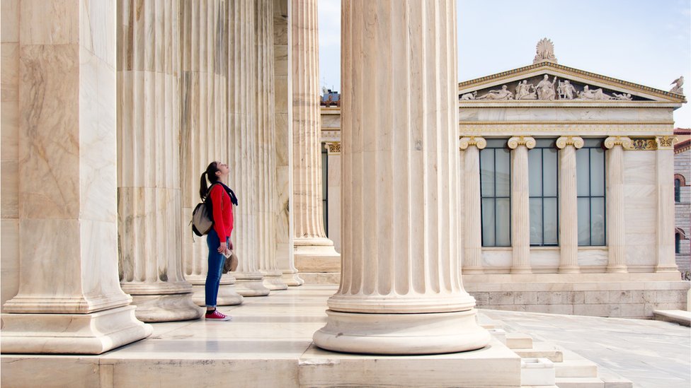 Una chica mira debajo de las columnas de la Academia Ateniense.