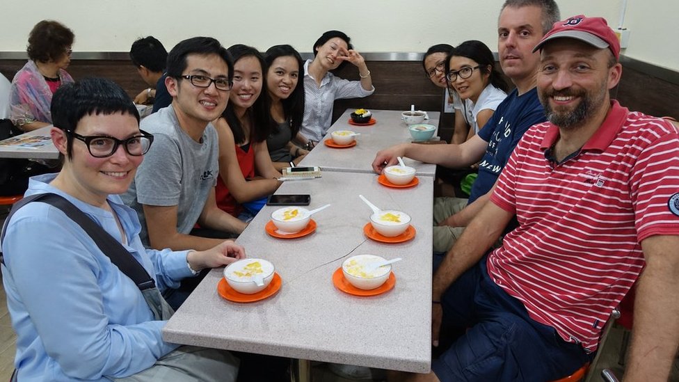 Paul Chan sentado en una mesa con turistas, con tazones de postre tradicional en 2015