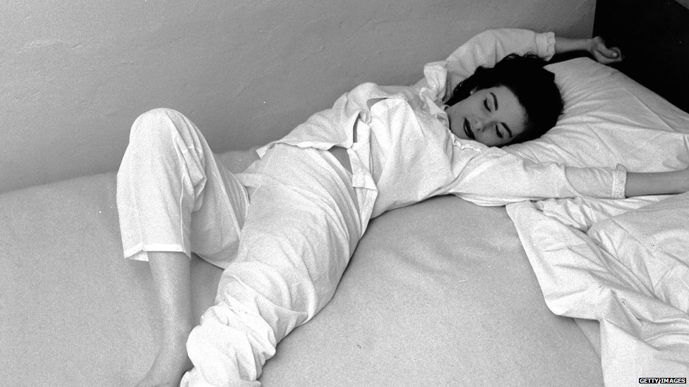 Черно-белое фото женщины в пижаме, растягивающейся на кровати