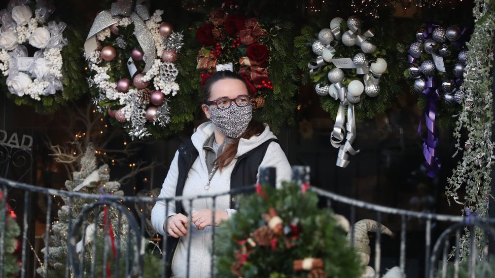 Человек с закрывающим лицо гуляет мимо рождественских венков, выставленных на продажу в цветочном магазине All Occasions Designer в Денни.