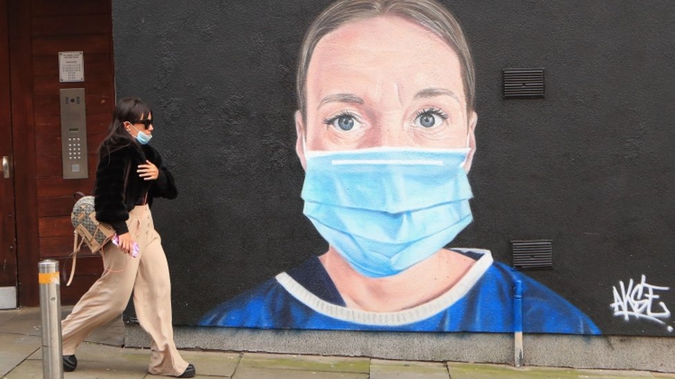 Женщина проходит мимо фрески с изображением сотрудника Национальной службы здравоохранения в центре Манчестера