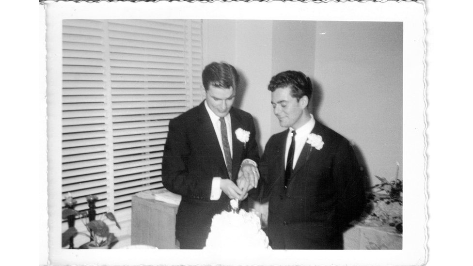 Dos hombre cortan un pastel de bodas.