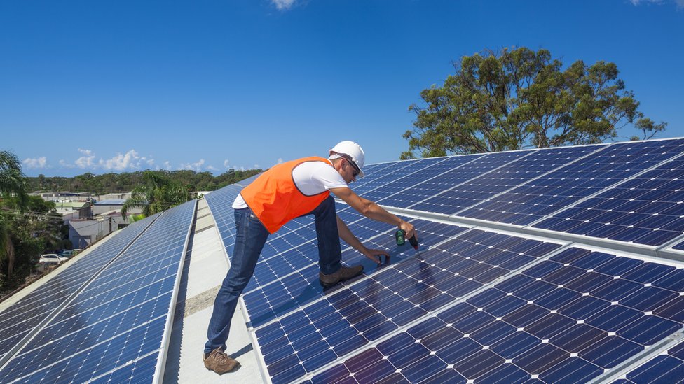 Hombre sobre tejado repleto de paneles solares.