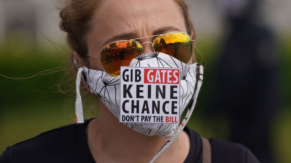 Una mujer lleva un cartel que dice: "No le des una oportunidad a Gates. No pagues la cuenta" en referencia a Bill Gates,