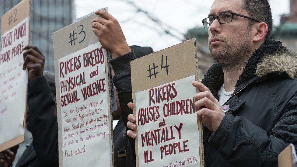 Протестующие держат таблички с указанием причин закрыть Rikers