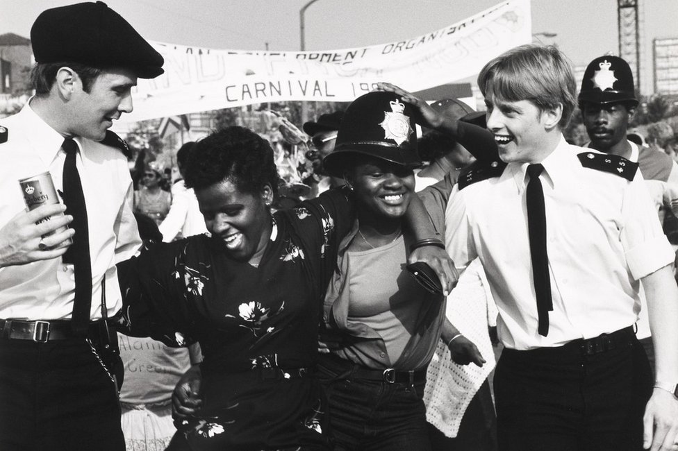 Два полицейских в форме танцуют с двумя любителями карнавала на карнавале в Ноттинг-Хилл, 1980-е