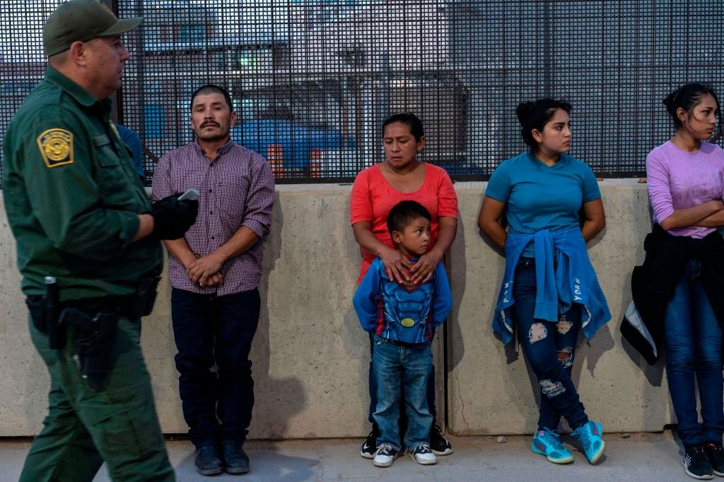 Мигранты, в основном из Центральной Америки, ждут, чтобы сесть в фургон, который отвезет их в центр обработки