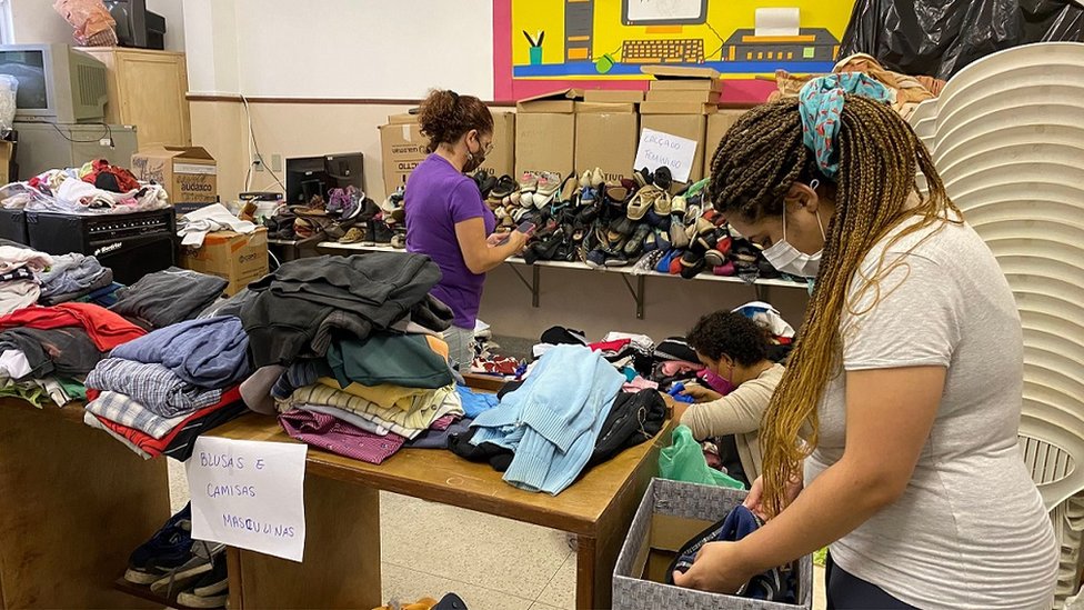 Duas mulheres de máscaras organizando sapatos e roupas em sala