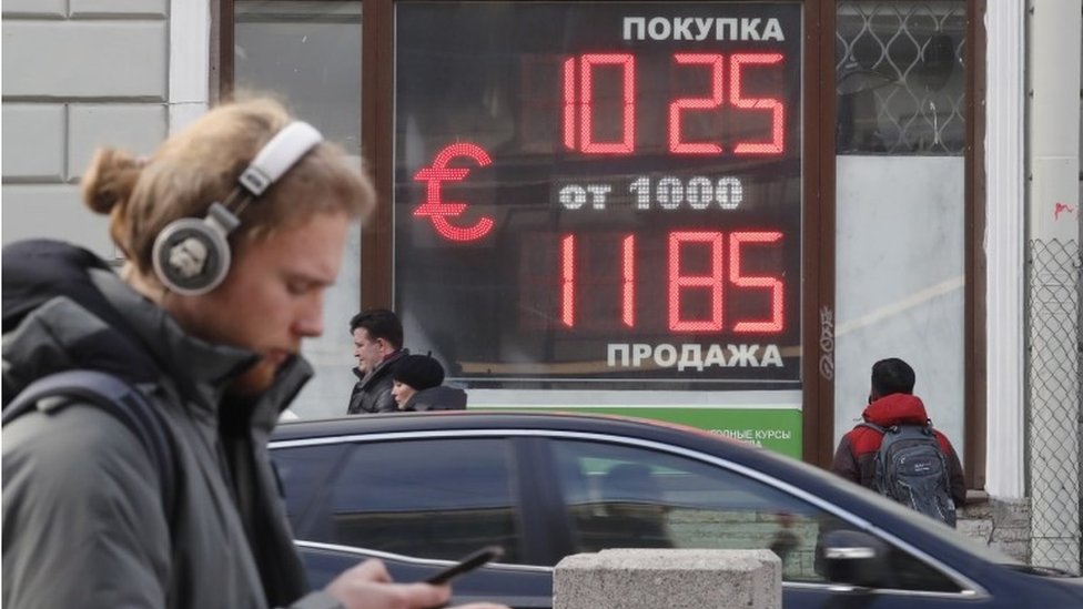 La gente pasea frente a un panel digital en el que se muestra el intercambio del rublo con el dólar y el euro, en San Petesburgo, el 28 de febrero.