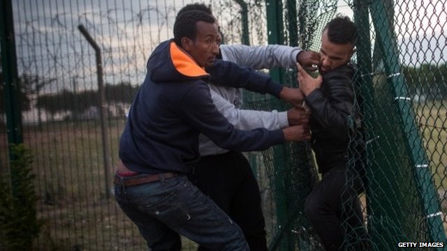 Migrants squeeze through a gap in a fence near the Eurotunnel terminal in Calais