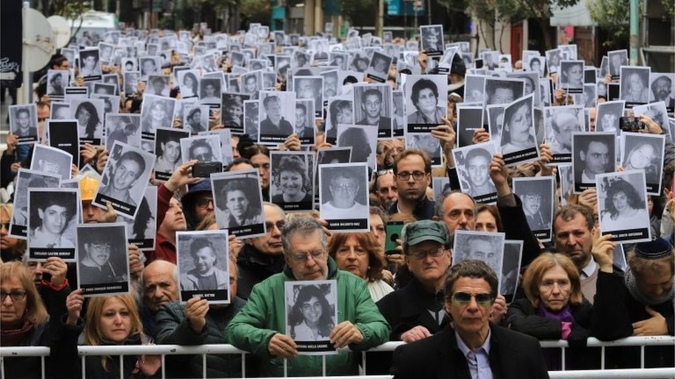 Фотография, опубликованная Noticias Argentinas, на которой изображены люди с фотографиями жертв взрыва бомбы в еврейском общинном центре Аргентинской ассоциации израильтян (AMIA) в 1994 году, в результате которого погибли 85 и ранены 300 человек, во время празднования 25-й годовщины нападения в Буэнос-Айресе в июле 18, 2019.
