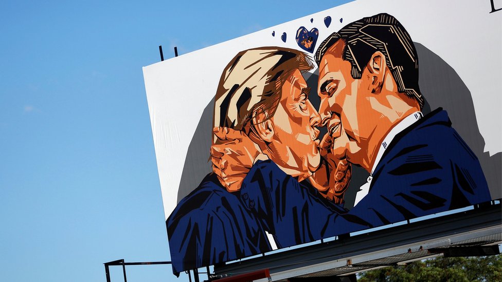 Рекламный щит, установленный перед Национальным съездом республиканцев, изображает кандидата в президенты США от республиканцев Дональда Трампа, целующего бывшего кандидата в президенты сенатора Теда Круза - июль 2016 г.