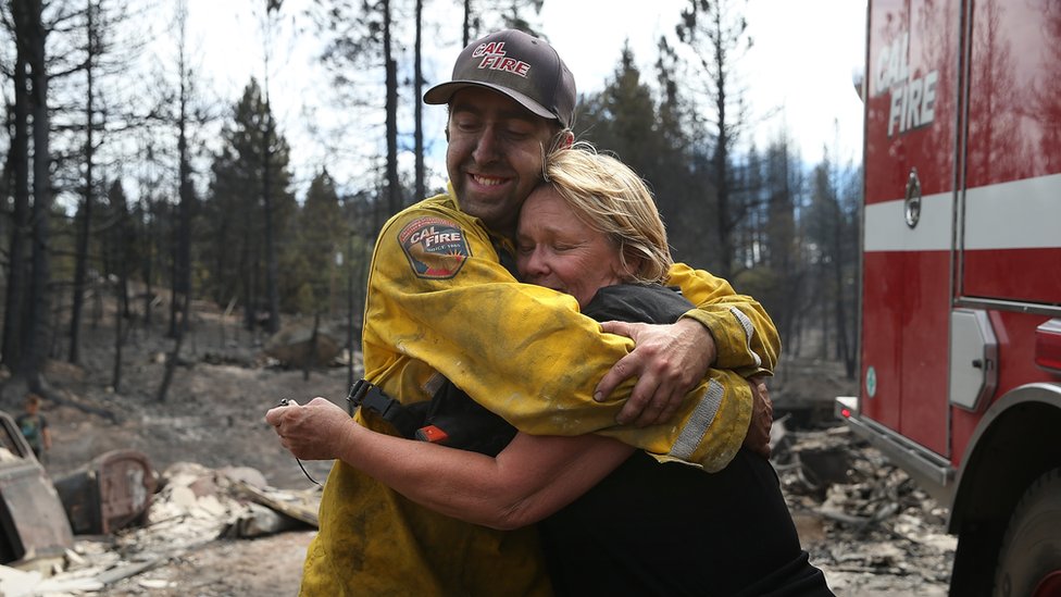 Кэти Беск (справа) обнимает пожарного CalFire Томми Яноу (слева) после того, как он обнаружил три ее кольца в сгоревших руинах ее дома