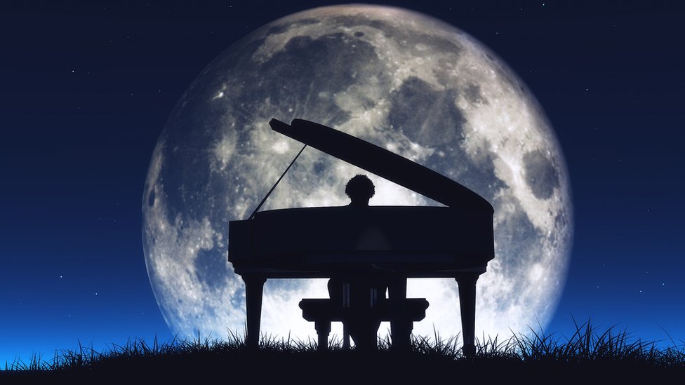 Persona tocando piano con la luna grande detrás.