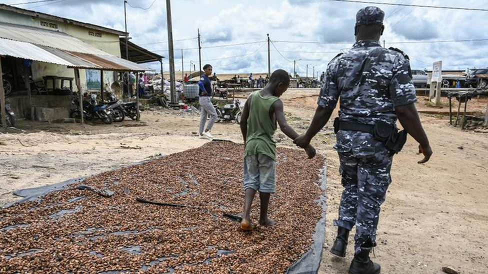 Um policial leva uma criança que trabalhava em uma instalação de processamento de cacau da Costa do Marfim durante uma operação