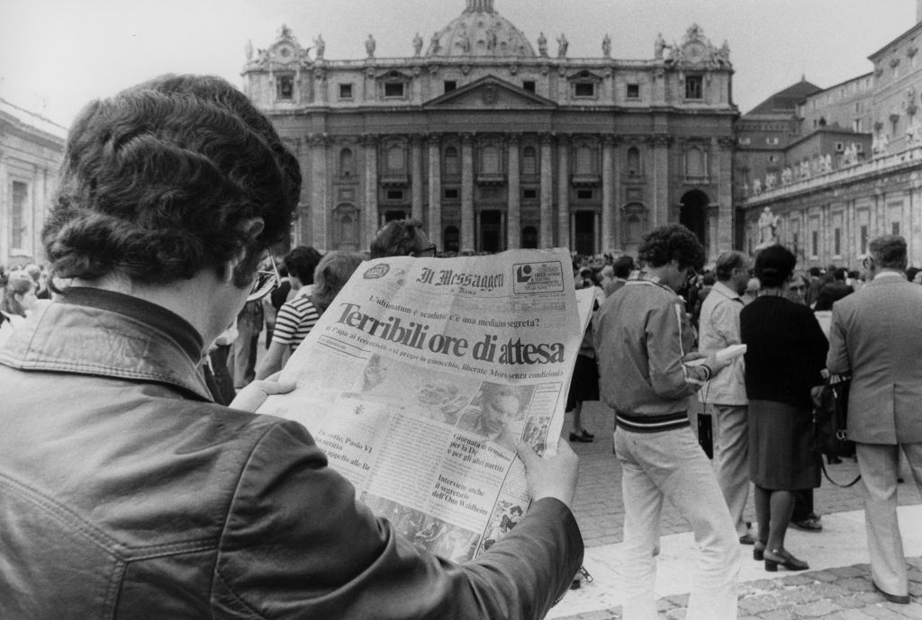 Un hombre lee un periódico en la plaza de san Pedro del Vaticano.